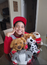 Jesus Rojas Petit smiling with a red hat and outfit Infront of stuffed animals 
